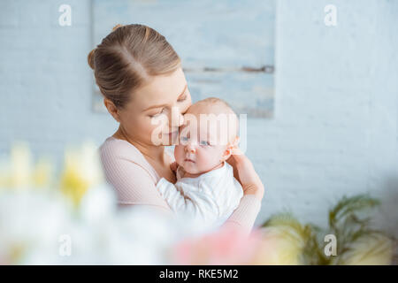 Selektiver Fokus der glückliche junge Mutter umarmt adorable Baby zu Hause Stockfoto