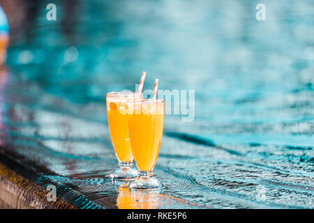 Zwei orange cocktails Gläser mit strohhalmen stehen am Pool Stockfoto