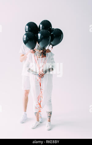 Freund und Freundin versteckt sich hinter schwarzen Luftballons auf grauem Hintergrund Stockfoto