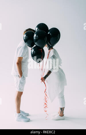 Mann und Frau versteckt sich hinter schwarzen Luftballons auf grauem Hintergrund Stockfoto