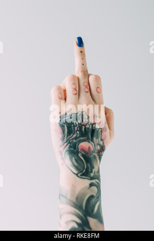 7/8-Ansicht von Frau mit Tattoos zeigt Mittelfinger isoliert auf Grau Stockfoto