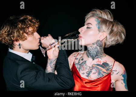 Die Frau im roten Kleid und der Mann mit dem lockigen Haar trinken Champagner isoliert auf Schwarz Stockfoto