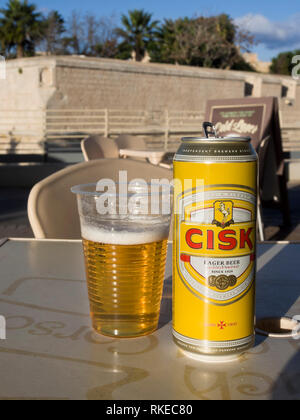 Ein kann der lokalen Lagerbier Marke Cisk und einem Kunststoff Glas in einer Ope-Bar in Malta mit der stadtbefestigung von Mdina im Hintergrund Stockfoto