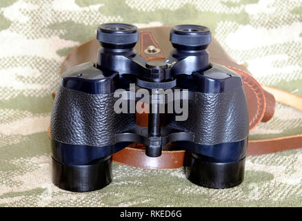 Vintage Englisch militärischen Prism schwarz Fernglas und braunem Leder Tragetasche mit Gurt auf Tarnung Hintergrund Vorderansicht Nahaufnahme Stockfoto