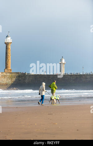 Whitby, Yorkshire, UK. 11. Februar, 2019. Großbritannien Wetter. Whitby, North Yorkshire, England. 11. Februar 2019. Die Besucher der North Yorkshire coast in Whitby genießen einen hellen, aber kalt Spaziergang entlang der Küste mit den alten Leuchtturm und Hafen im Hintergrund. Alan Beastall // Alamy leben Nachrichten Stockfoto