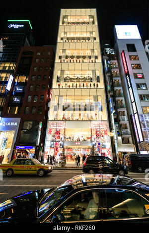 Tokyo Ginza, Nacht. Über street view von Flagship Glasfassade Uniqlo 12 Geschichte store beleuchtet. Taxi im Vordergrund. Weihnachtsbäume auf Pflaster. Stockfoto