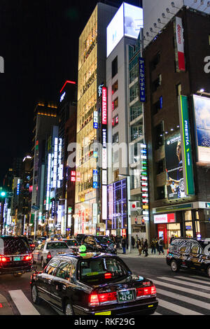 Tokyo Ginza, Nacht. Flaggschiff Glasfassade der Uniqlo, 12-stöckiges Hochhaus Store unter anderem Geschäfte entlang der Straße. Taxi im Vordergrund. Stockfoto