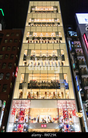 Tokyo Ginza, Nacht. Über street view von Flagship Glasfassade Uniqlo 12 Geschichte store beleuchtet. Taxi im Vordergrund. Weihnachtsbäume auf Pflaster. Stockfoto