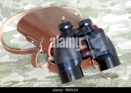 Vintage Porro Farbe schwarz Militär Fernglas und braunem Leder Tragetasche mit Gurt auf Tarnung Hintergrund Seitenansicht Nahaufnahme Stockfoto