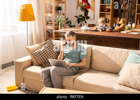 Besetzt Vater zu Hause arbeiten, während Sohn gebohrt werden Stockfoto