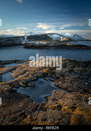 Atlantic Ocean Road - Atlanterhavsvegen im Winter sonniger Tag. Berühmte hohe Brücke über das Meer genannt Storseisundbrua und schöne verschneite Berge in einer Stockfoto