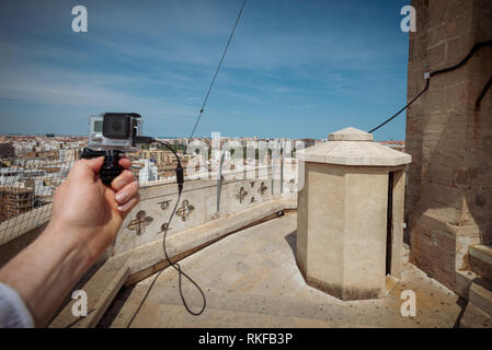Ein Mann hält eine GoPro Kamera vor der Aussicht auf die Stadt an der Spitze der El Miguelete, der Glockenturm der Kathedrale von Valencia in Valencia Stockfoto