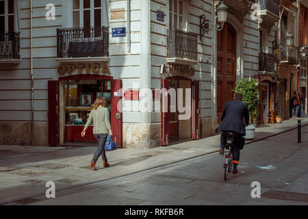 Ein Mann Zyklen Vergangenheit eine Frau, als sie Spaziergänge entlang einer Straße in der Altstadt von Valencia, Spanien. Stockfoto