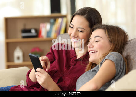 Zwei glückliche Mitbewohner Kontrolle smart phone Inhalt auf einer Couch im Wohnzimmer zu Hause sitzen Stockfoto