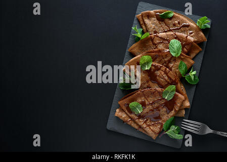 Hausgemachte Schokolade Pfannkuchen mit Heidelbeeren, Soße und Minze auf schiefer Teller serviert. Selektive konzentrieren. Ansicht von oben. Platz kopieren Stockfoto