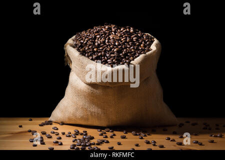Close up geröstete Kaffeebohnen in einem sackleinen hessische Sack und isoliert in Schwarz. Stockfoto