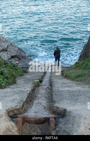 Ein Mann stand am unteren Ende der alten stillgelegten Newquay Rettungsboot Slipway. Die historische Slip hat die steilste Steigung starten in England. Stockfoto