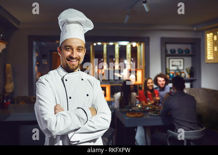Ein männlicher Cook ist lächelnd vor dem Hintergrund der ein Restaurant. Stockfoto