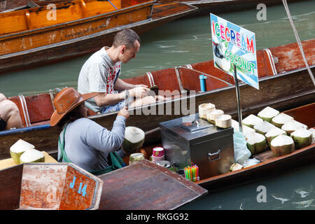 Damnoen Saduak - 4. März 2014: Ein Mann kauft eine Kokosnuss von einem Anbieter. Der schwimmende Markt ist sehr berühmt. Stockfoto