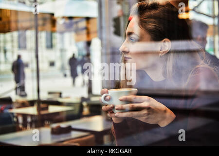 Mädchen träumen während hält eine Tasse Kaffee im Café, Konzept Foto durch Fenster zur Stadt Wirkung mit Reflektion Stockfoto