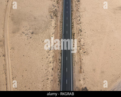 Luftaufnahme von einer Straße in die Wüste, Radfahrer Racing auf dem Fahrrad auf dem schwarzen Asphalt. Outdoor Sport, Radfahren, Tourismus. Lanzarote, Spanien Stockfoto