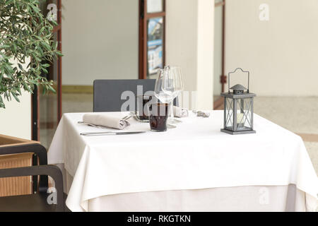 Eine leere Tabelle für Zwei in einem Restaurant, mit einer weißen Tischdecke mit zwei Tisch Sets und eine Laterne bedeckt, in einem Café oder Restaurant außerhalb. Stockfoto