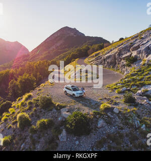 Paar in der Nähe von weißen suv-Auto auf der Flanke des Hügels. Luftaufnahme Stockfoto