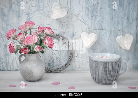 Valentines Tag Stillleben mit Rosen, Tasse heiße Schokolade und girlande Lichter in Form von Papier Herzen auf rustikalen Hintergrund Stockfoto