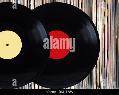 Zwei schwarzen Schallplatten mit Farbe Etiketten vor Haufen von vielen nahe stehenden Schallplatten in der alten Farbe deckt über schwarzen Hintergrund studio Shot Stockfoto