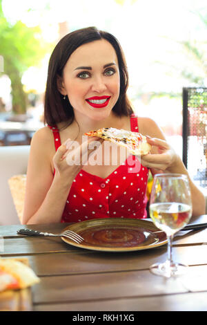 Schöne junge lächelnde Frau isst ein Stück Pizza im Restaurant im Freien Stockfoto