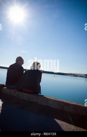 Hintere Aufnahme eines älteren Paares diskutieren, sitzen auf einem Meer mit Blick auf einen ruhigen Hafen an einem sonnigen Wintertag in Cahors, Frankreich Stockfoto