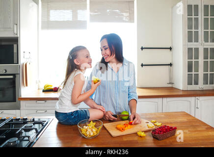 Schöne Mädchen mit ihrer Mutter in der Küche vorbereiten Ein frischer Obstsalat in der Küche Stockfoto