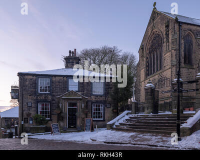 Haworth, West Yorkshire, der Heimat der Bronte Familie, der Stier Public House von Patrick Bronte und die Pfarrkirche, im Winter mit Schnee besucht. Stockfoto
