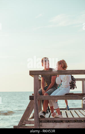 Glücklich lächelnde Paar der jungen Frau und Mann sitzt auf einem Pier über das Meer im Sommer Ferien. Kopieren raum raum für Text Stockfoto