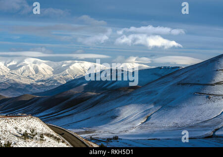 Blick auf die scharfen Kurven auf dem Weg in die Stadt von Spitak und die ersten Strahlen der Wintersonne, Streuung der Nebel in den Bergen des Aragats Stockfoto