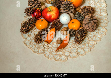 Wellenförmige bestickte Servietten mit Apple, Mandarinen, Nüsse, Mandeln, Weihnachtskugeln und verschiedene Tannenzapfen auf Sperrholz Stockfoto