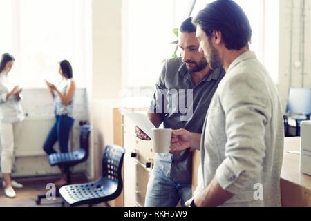 Nette Kaffeepause. Zwei fröhliche junge Menschen halten Kaffeetassen und Reden, während im Büro stehen. Stockfoto