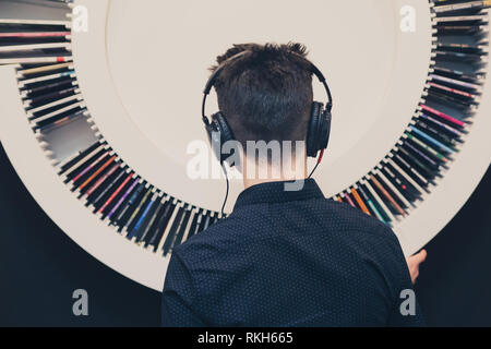 Junger Mann Hören von Musik über Kopfhörer neben mit Aufnahmen zum Bücherregal Stockfoto