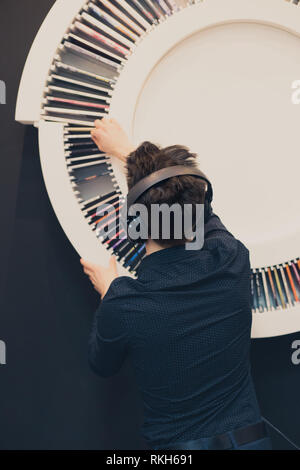 Junger Mann Hören von Musik über Kopfhörer neben mit Aufnahmen zum Bücherregal Stockfoto