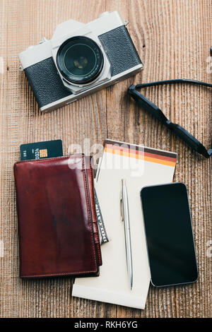 Mit leerer Bildschirm, Kamera, Tasche, Dollar, Banknoten, Smartphone, Debit Kreditkarten und Notebook auf hölzernen Tisch. Blick von oben. Hochformat Stockfoto