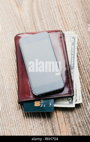 Mit leerer Bildschirm, Portemonnaie, Dollar, Banknoten, Smartphone, Debit Kreditkarten und Notebook auf hölzernen Tisch. Blick von oben. Hochformat Stockfoto