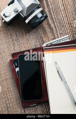 Mit leerer Bildschirm, Kamera, Tasche, Dollar, Banknoten, Smartphone, Debit Kreditkarten und Notebook auf hölzernen Tisch. Blick von oben. Hochformat Stockfoto