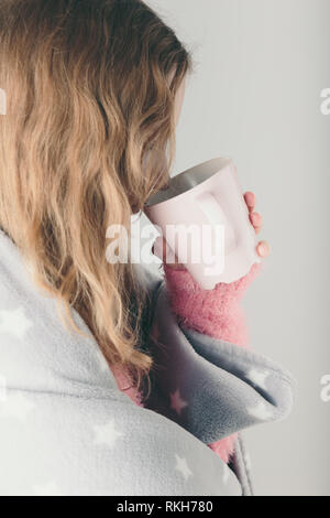 Junge Frau kalt erwischt hat, Tag, kranken Tag, in der Decke eingewickelt, hält Tasse Kräutertee. Profil Hochformat Stockfoto