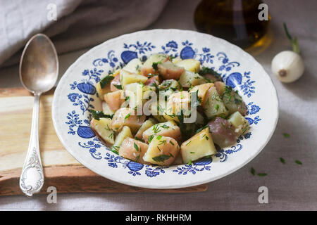 Traditionelle kalte Kartoffelsalat mit Zwiebeln und Kräutern auf einem Leinen Tischdecke Hintergrund. Im rustikalen Stil. Stockfoto