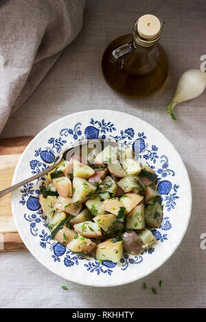 Traditionelle kalte Kartoffelsalat mit Zwiebeln und Kräutern auf einem Leinen Tischdecke Hintergrund. Im rustikalen Stil. Stockfoto