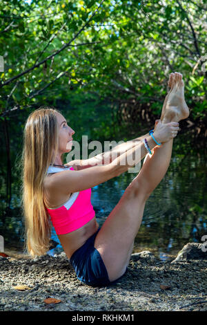 Junge Frau mit Yoga (modifizierte Boot Pose-Navasana) in einer natürlichen Umgebung - Fort Lauderdale, Florida, USA Stockfoto