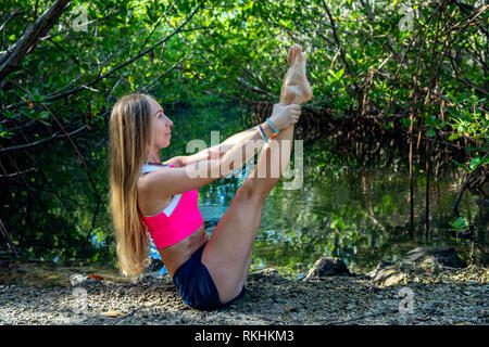 Junge Frau mit Yoga (modifizierte Boot Pose-Navasana) in einer natürlichen Umgebung - Fort Lauderdale, Florida, USA Stockfoto