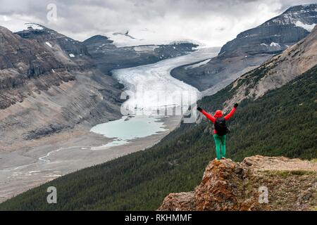 Wanderer steht auf einem Felsen, streckt die Arme in die Luft, in das Tal mit Blick auf die Gletscherzunge, Parker Ridge, Saskatchewan Gletscher, Stockfoto