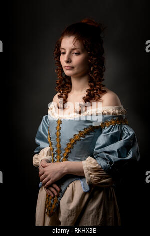 Attraktive junge Dame in wunderschönen barocken Kleid halten die Hände auf Bauch beim Stehen auf schwarzem Hintergrund Stockfoto