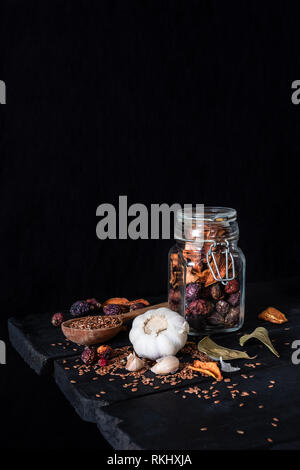 Knoblauch, getrocknete Früchte und Samen in dunklen rustikalen Hintergrund. Künstlerische Foto von Knoblauch und trockene Frucht in einem Glas auf alten Schwarzen Tisch Schuß in Low Key ciaroscurr Stockfoto